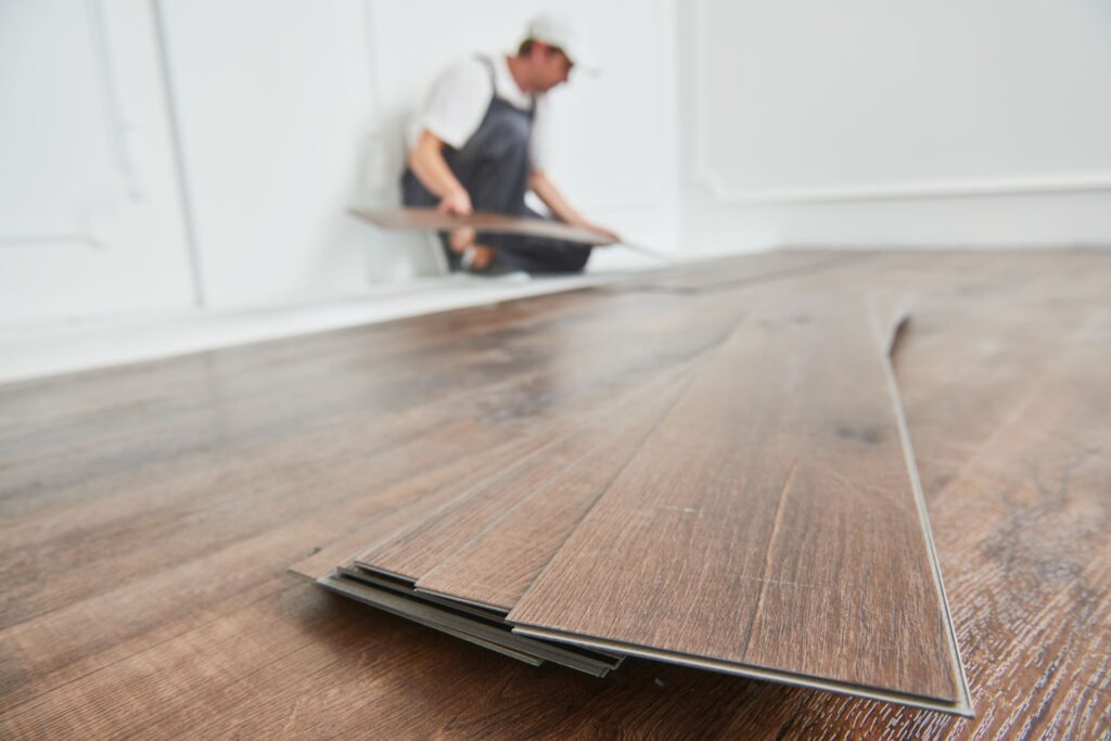 Nahaufnahme eines Handwerkers bei der Verlegung von Klick Vinyl Eiche Bodenbelägen, die eine einfache und schnelle Installation ermöglichen und gleichzeitig eine natürliche Holzoptik bieten.