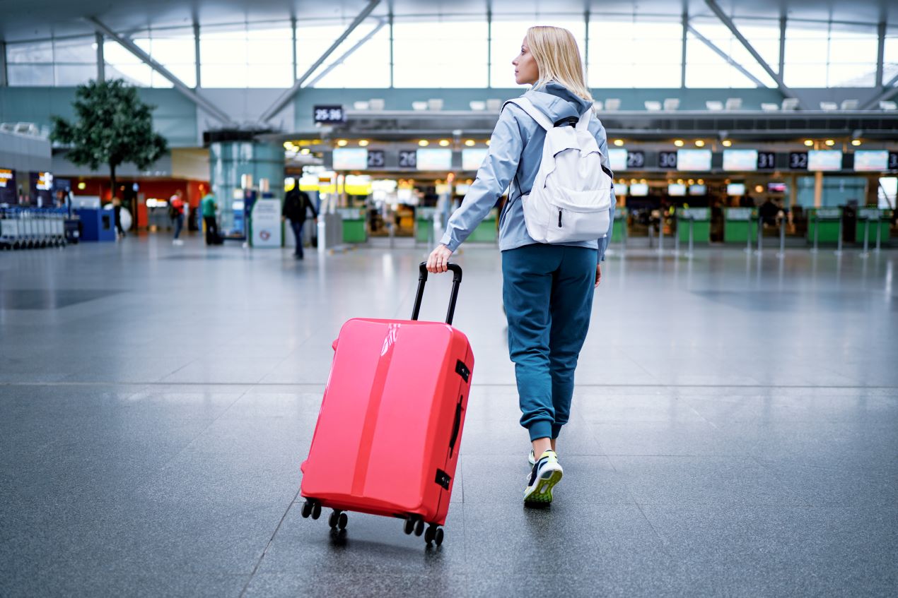 Eine Reisende zieht einen roten Koffer durch das moderne Flughafen-Terminal. Tipps und Organisation für Parken Flughafen Nürnberg.