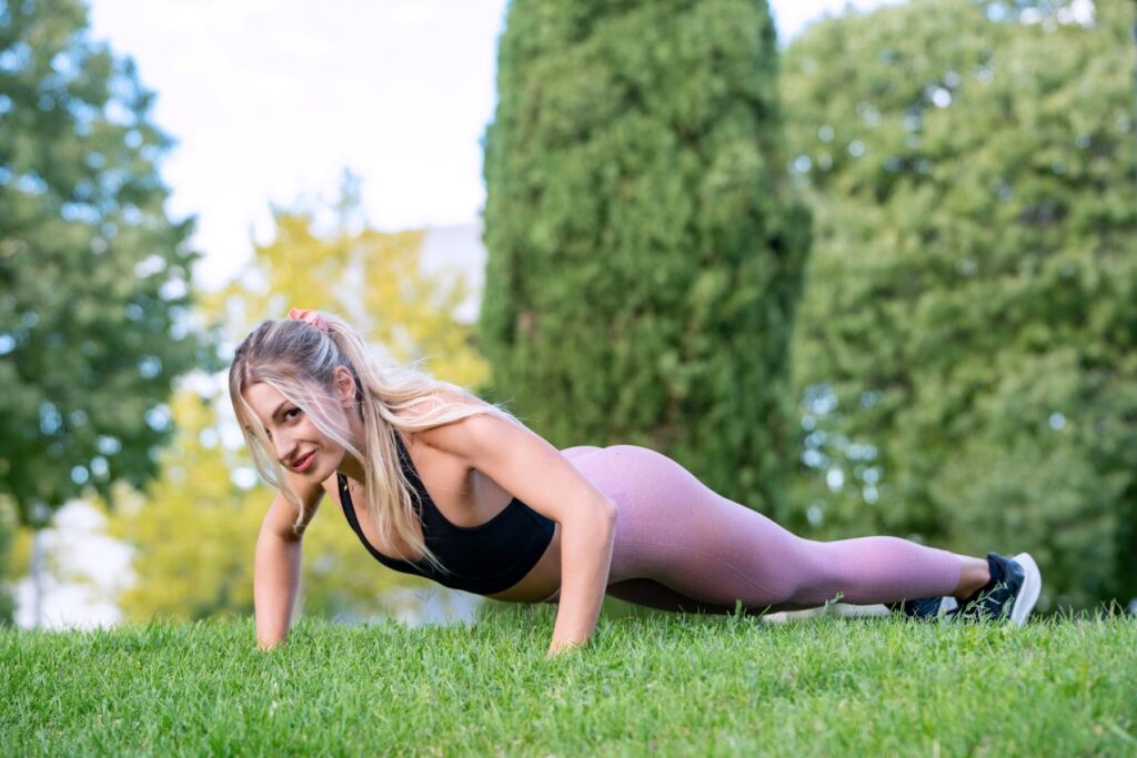 Junge Frau macht Outdoor-Liegestütze auf einer grünen Wiese – perfektes Training mit einem Personal Trainer in Köln.