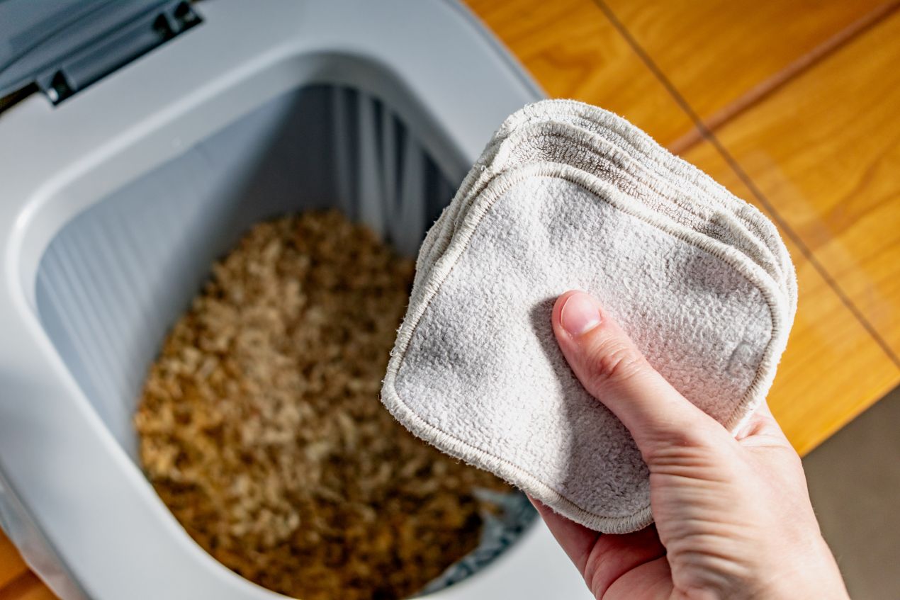 Hand hält waschbare Reinigungstücher vor einer Trockentoilette, als Symbol für nachhaltige Hygiene und umweltfreundliche Kreislaufwirtschaft.