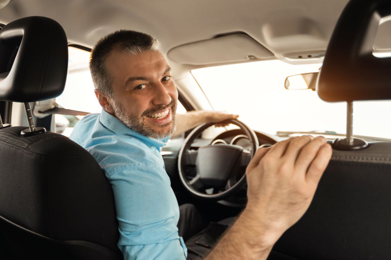Taxifahrer Jobs hautnah: Freundlicher Fahrer blickt rueckwaerts, bereit zur naechsten Fahrt – Symbolbild fuer mobile Berufe mit direktem Kundenkontakt