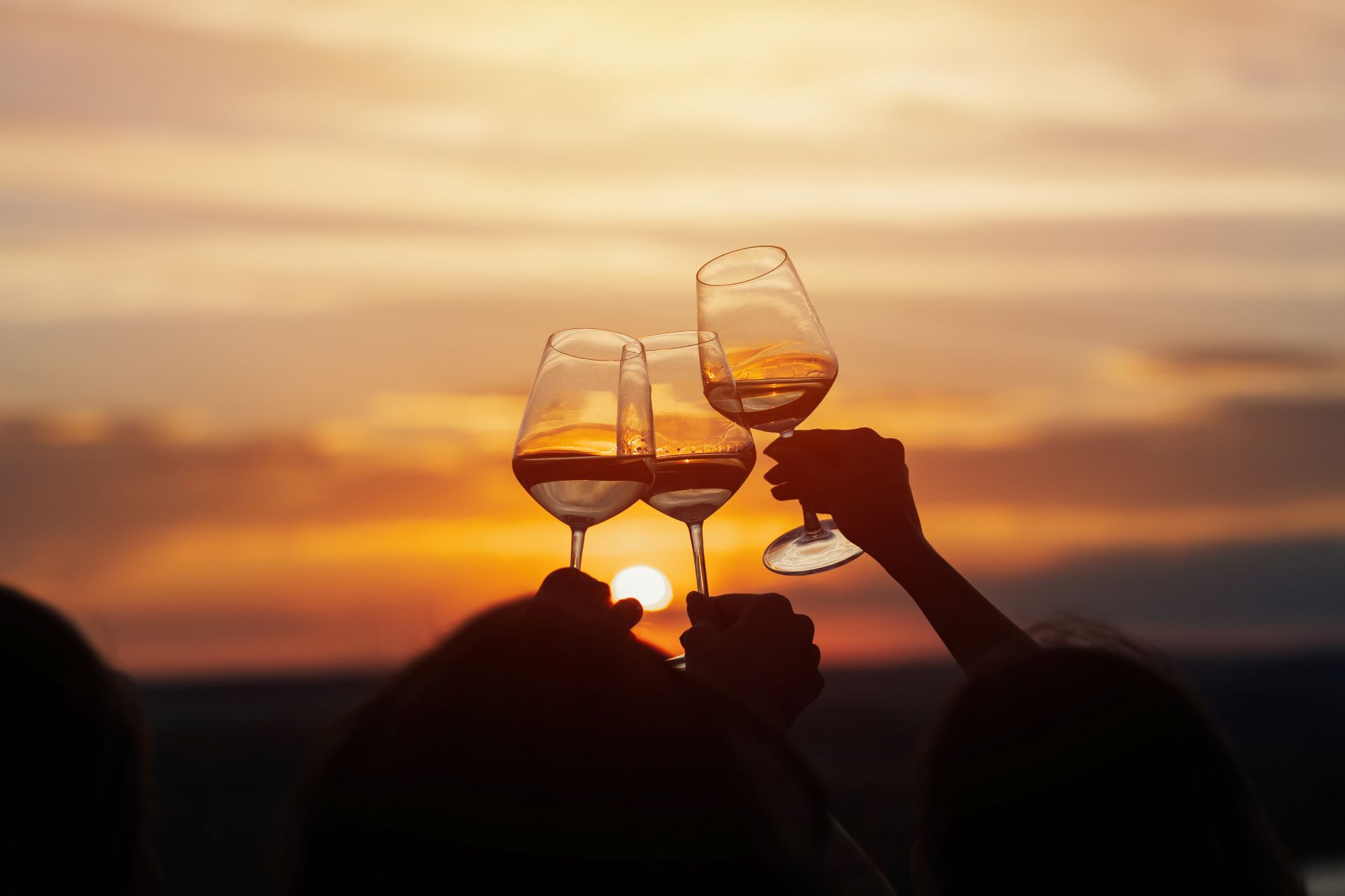 Drei erhobene Weinglaeser vor Sonnenuntergang in geselliger Runde