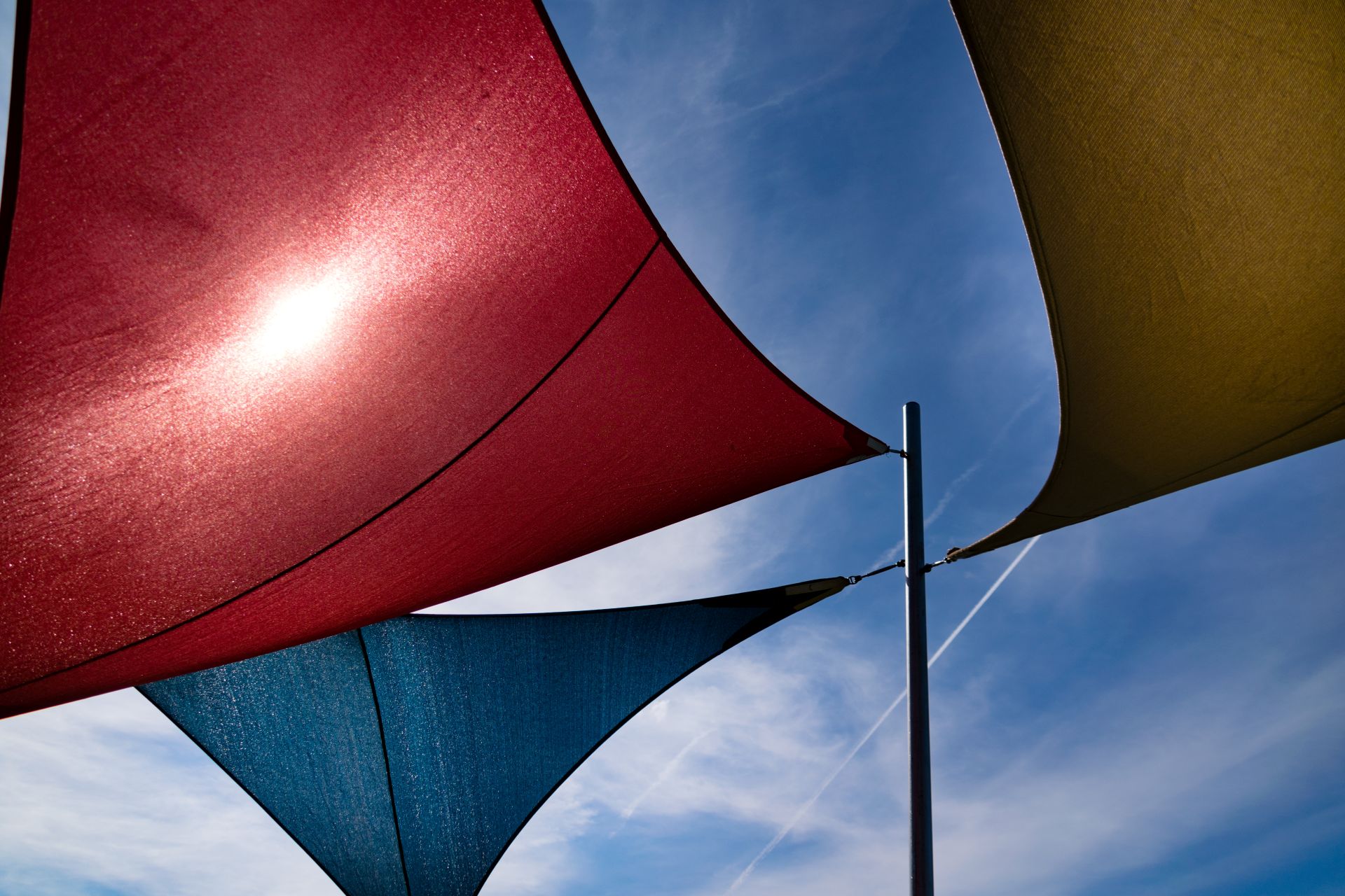 Dreieckige bunte Sonnensegel am Mast gegen blauen Himmel gespannt