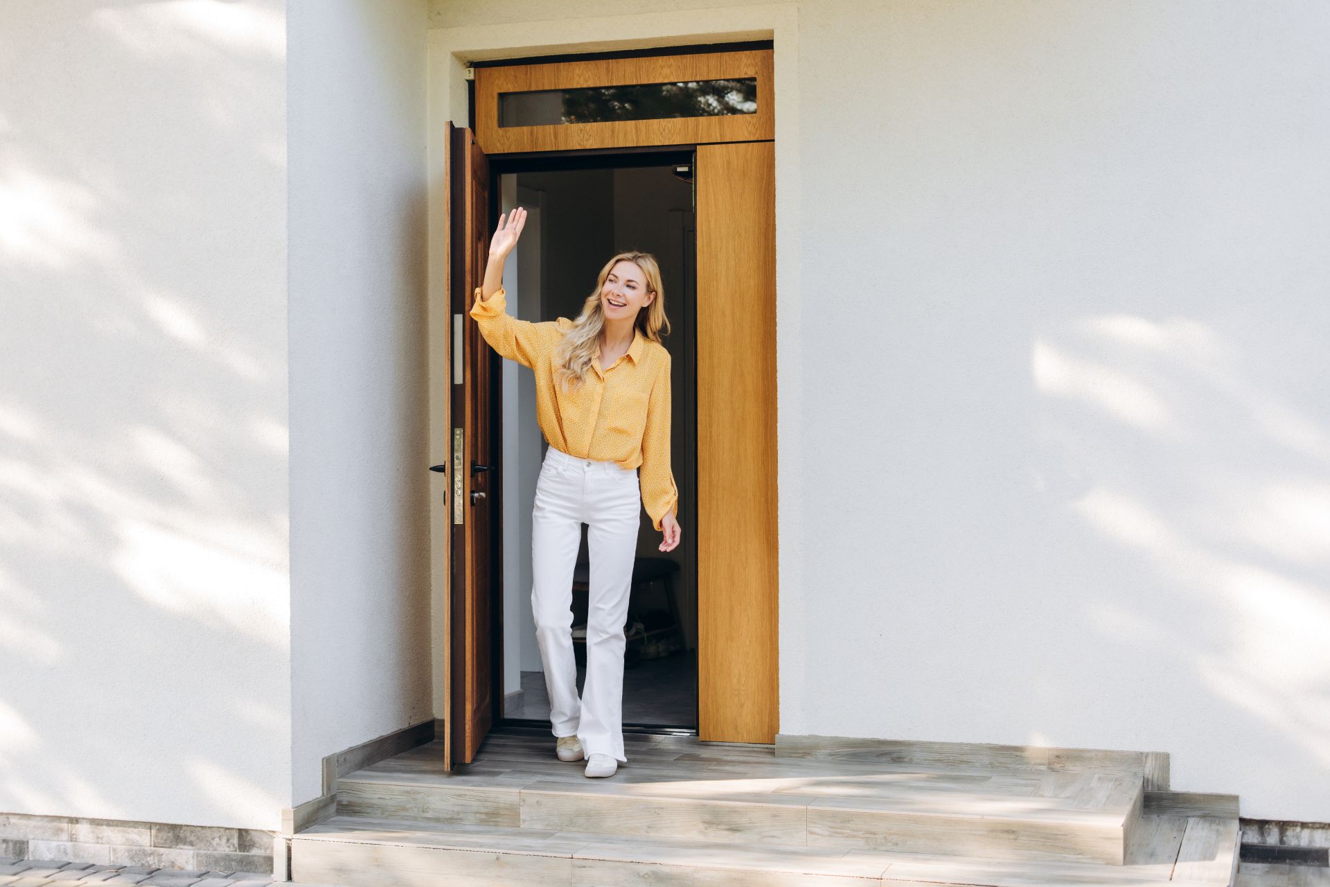 Frau begruesst Gaeste an einer modernen Holztuer vor ihrem Zuhause, Symbol fuer Haustueren Wuppertal